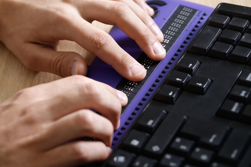 Hands typing on a purple braille keyboard