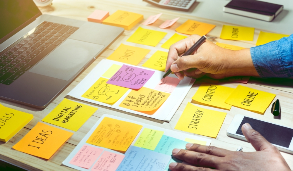 Hands writing on a table with several post-it notes with various words written on them