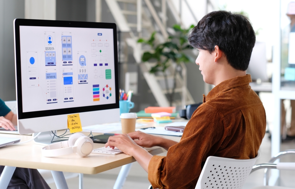 A web developer working on UI design layouts on a large monitor