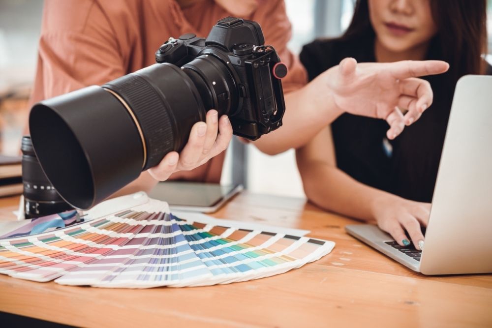 Two photographers, one holding a camera, discuss creative with a Pantone swatch book.