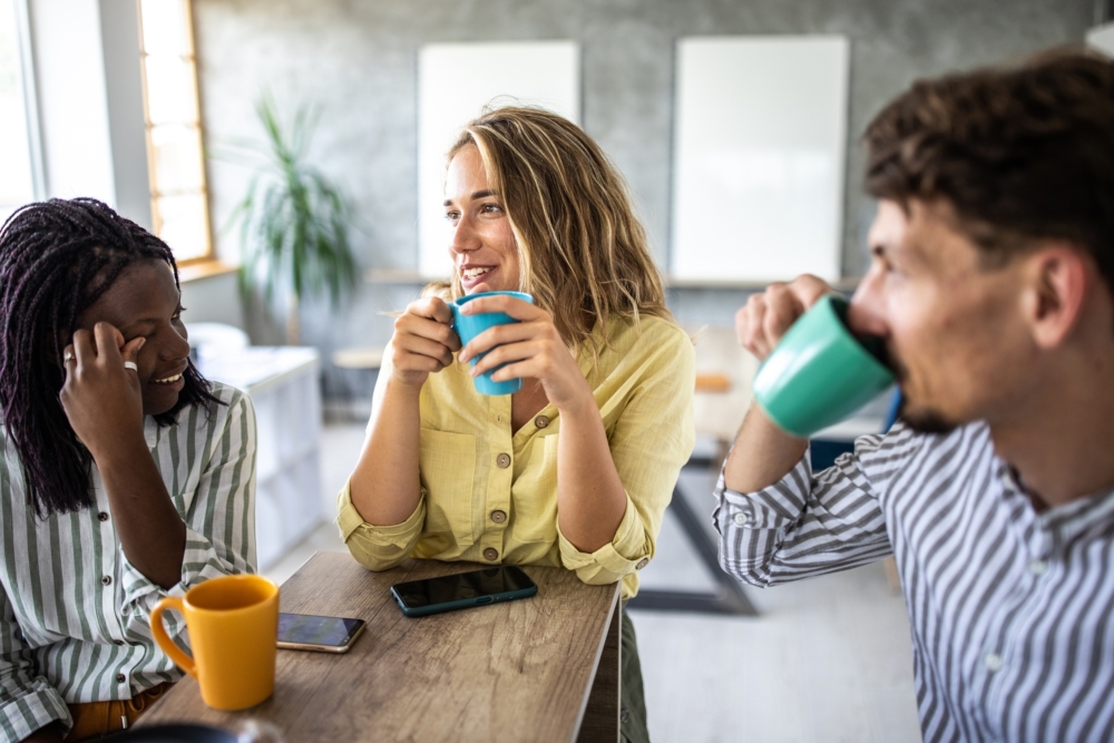 Three colleagues drinking coffee in a sunny office space