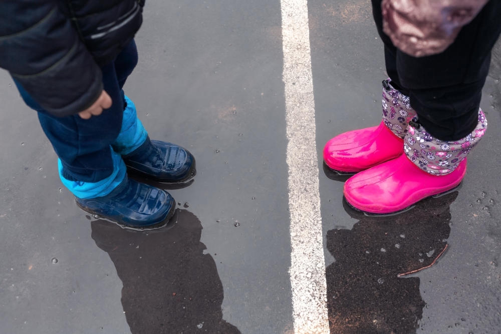 Two sets of childrens' boots, blue and pink, standing on either side of a white line