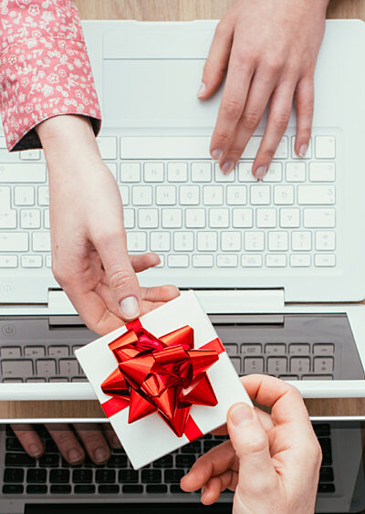 Person handing another person gift over two laptops on a desk