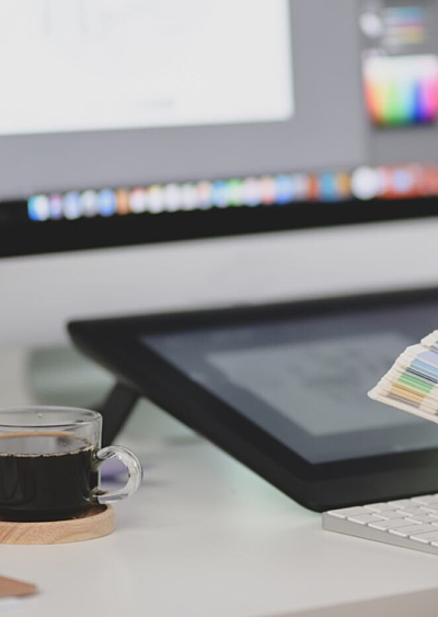 Hands sorting through colour palettes at a desk with design software on the monitor