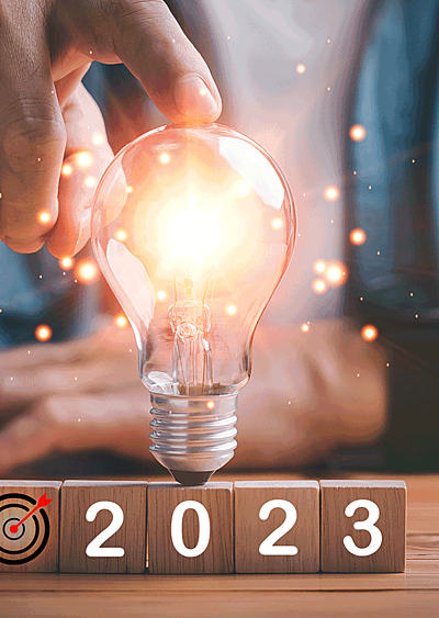 A man's hands point to a lightbulb over wooden blocks that spell '2023'