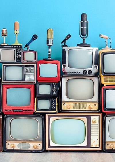An assortment of retro TV sets and microphones stacked in front of a blue wall