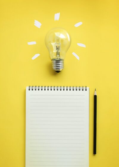 Flat lay of light bulb and empty notepad and pencil on yellow background.