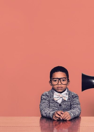 Child Yelling into a megaphone into another child's ear with red background