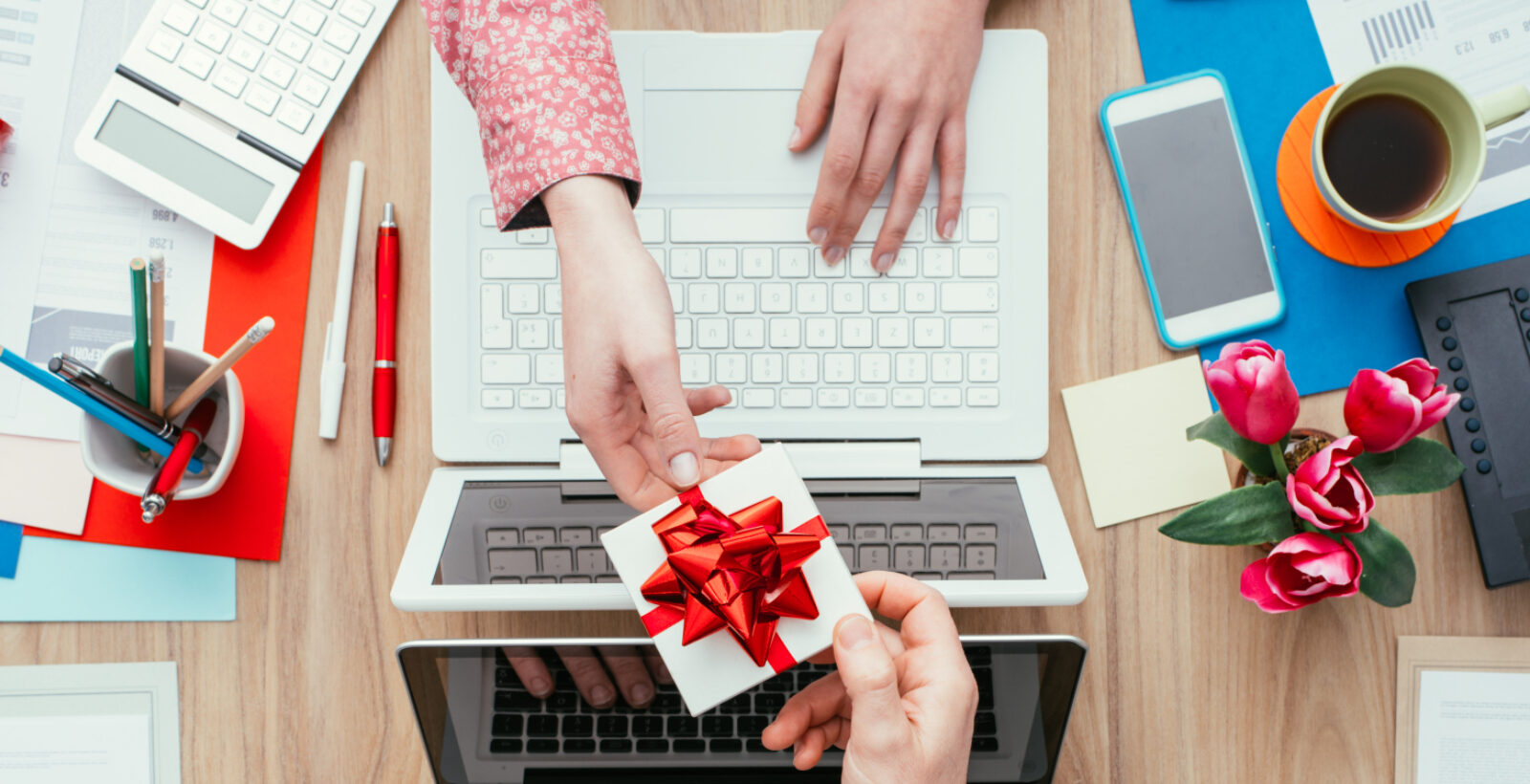 Person handing another person gift over two laptops on a desk