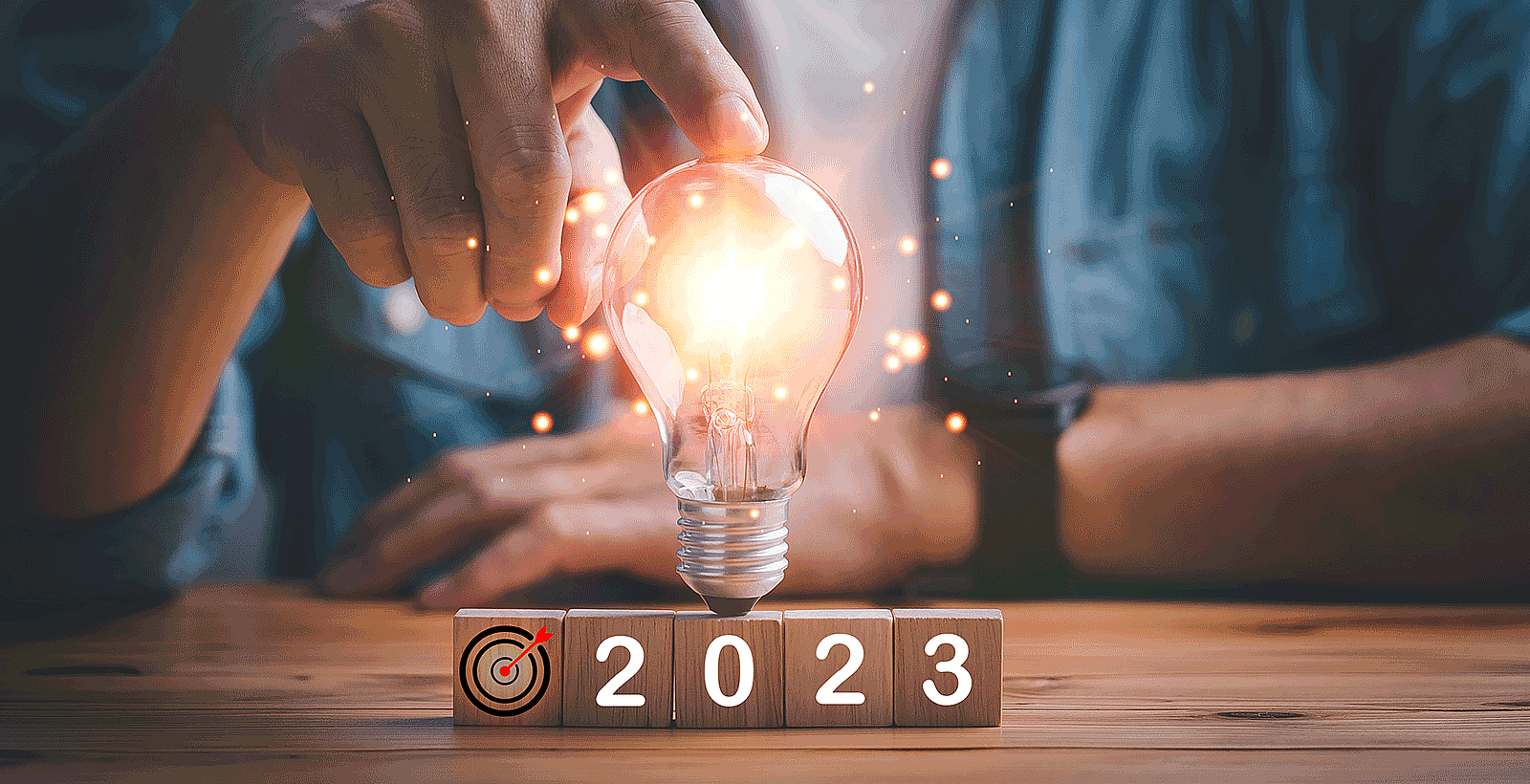 A man's hands point to a lightbulb over wooden blocks that spell '2023'