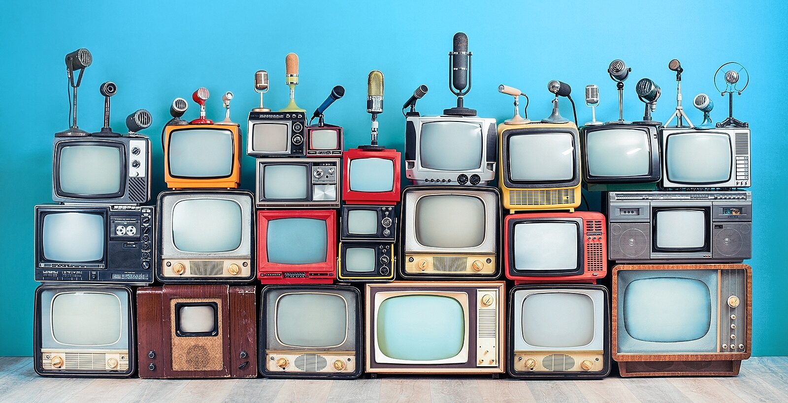 An assortment of retro TV sets and microphones stacked in front of a blue wall