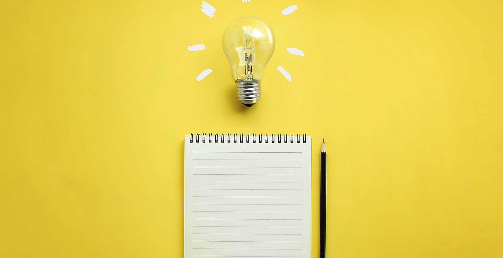 Flat lay of light bulb and empty notepad and pencil on yellow background.
