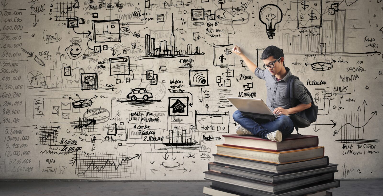 Student sitting on a stack of book with a laptop making graphics on wall